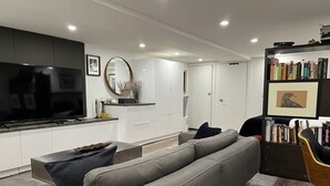 A modern living room with a grey sectional sofa, a black chair, a bookshelf, and a flat-screen TV.