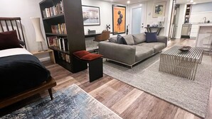 A modern living room with a sofa, a bookshelf, a coffee table, and a bed.