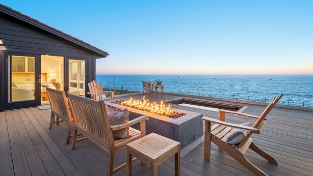 A deck with a fire feature, seating, and a view of the ocean. - Distinguished Oceanfront Point Estate with Iconic Beach + Mountain Vistas (Montara)
