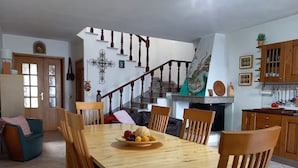 Uma área de refeições com mesa e cadeiras de madeira, uma fruteira e uma escada que leva a outro andar.