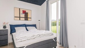 Ett modernt sovrum med en grå säng, vita sängkläder, ett svart tak och ett stort fönster med grå gardiner.