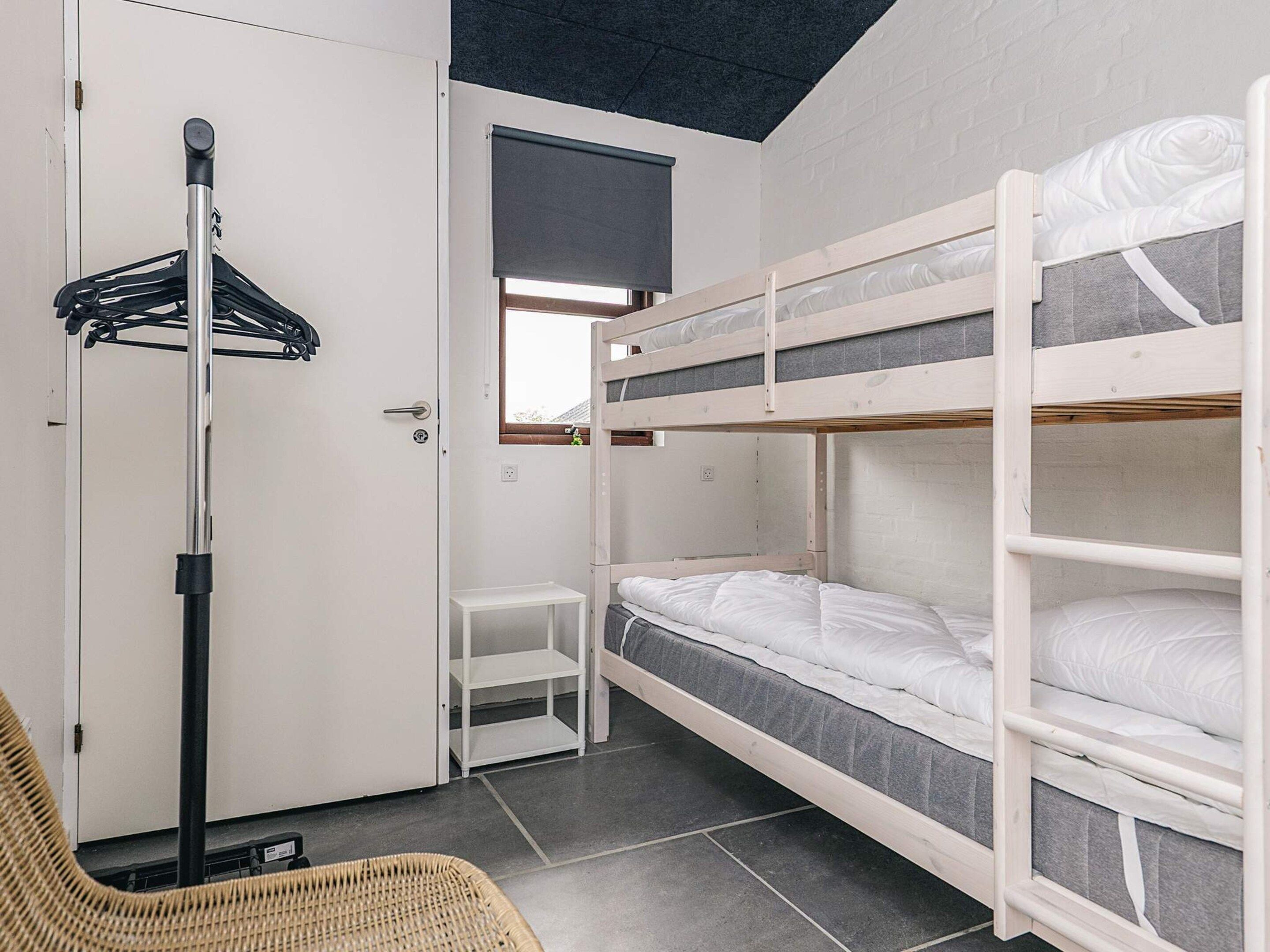 A bunk bed room with a door, a small table, a chair, and a standing lamp.
