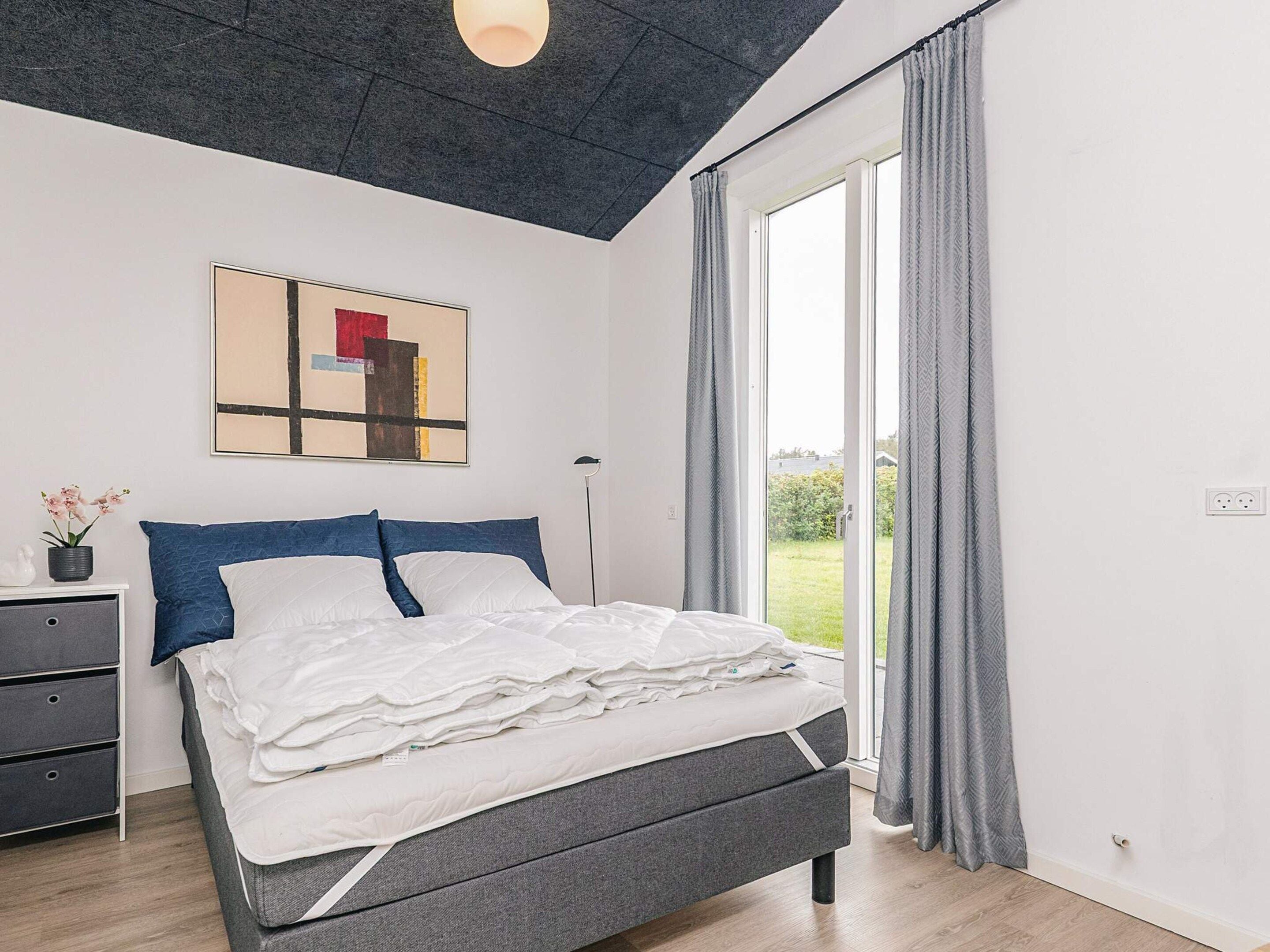 A modern bedroom with a bed, bedside table, and a large window with curtains.