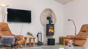 Ett mysigt vardagsrum med två läderfåtöljer, en platt-TV, en eldstad i sten och ett litet bord med växter.