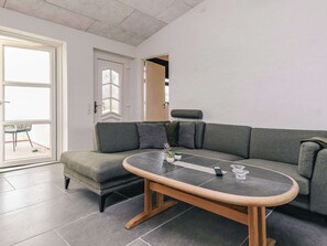 A modern living room with a grey sectional sofa, a glass-top coffee table, and a door leading to a balcony.