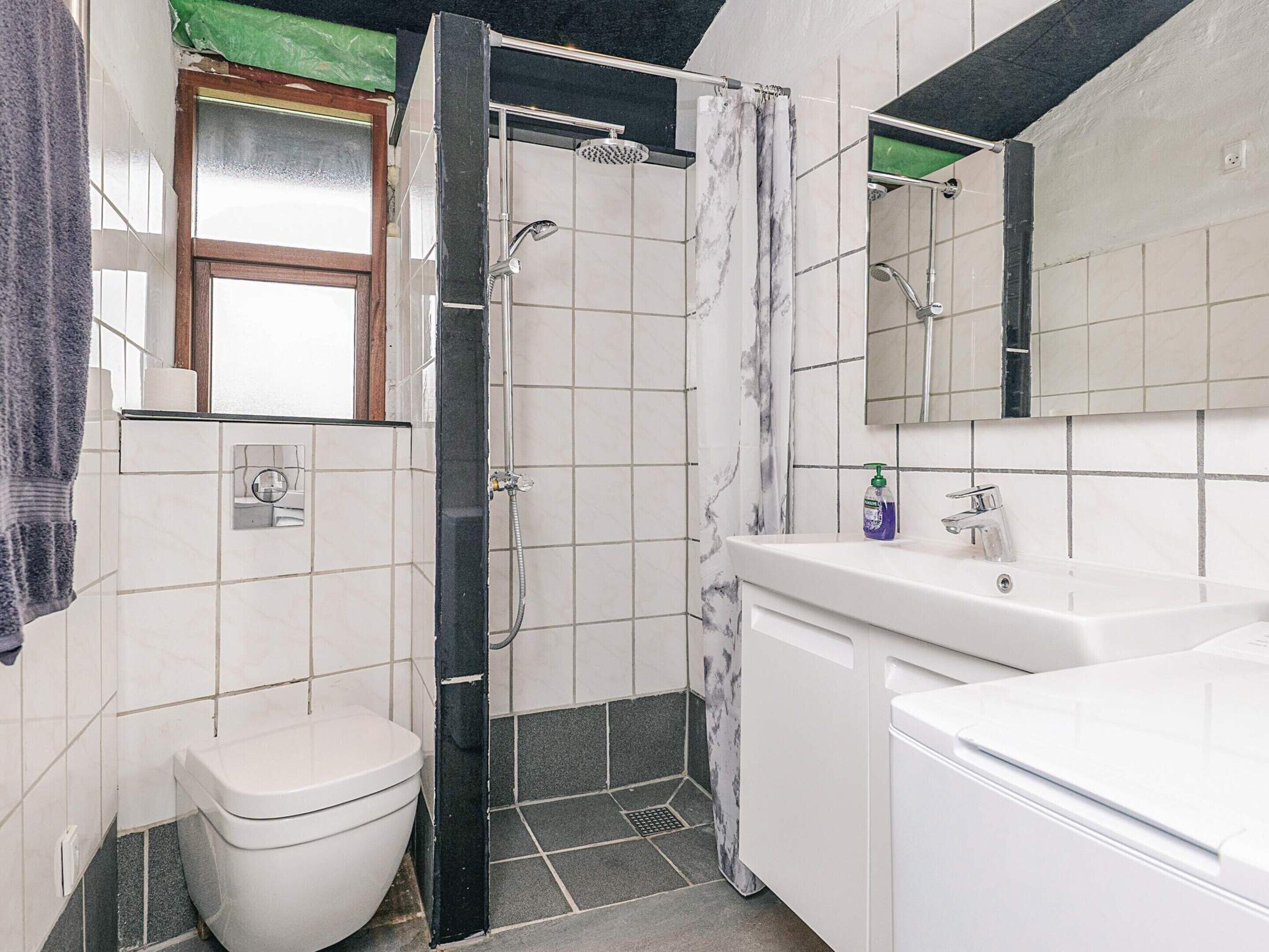 A bathroom with a toilet, sink, shower, and a mirror.