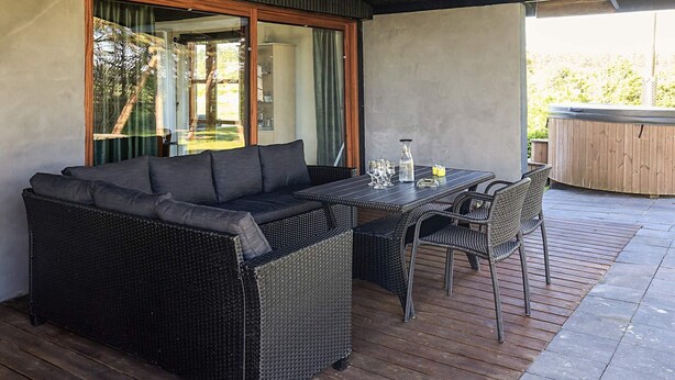Ett takförsett utomhusområde med sittplatser, en soffa och ett bord, ett bubbelbad och utsikt över omgivningen.
