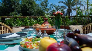 Mesa de comedor al aire libre con un tajín marroquí, platos, vasos y una ensalada.