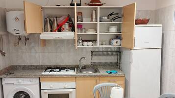 A compact kitchen with a washing machine, oven, and a dining area with chairs.