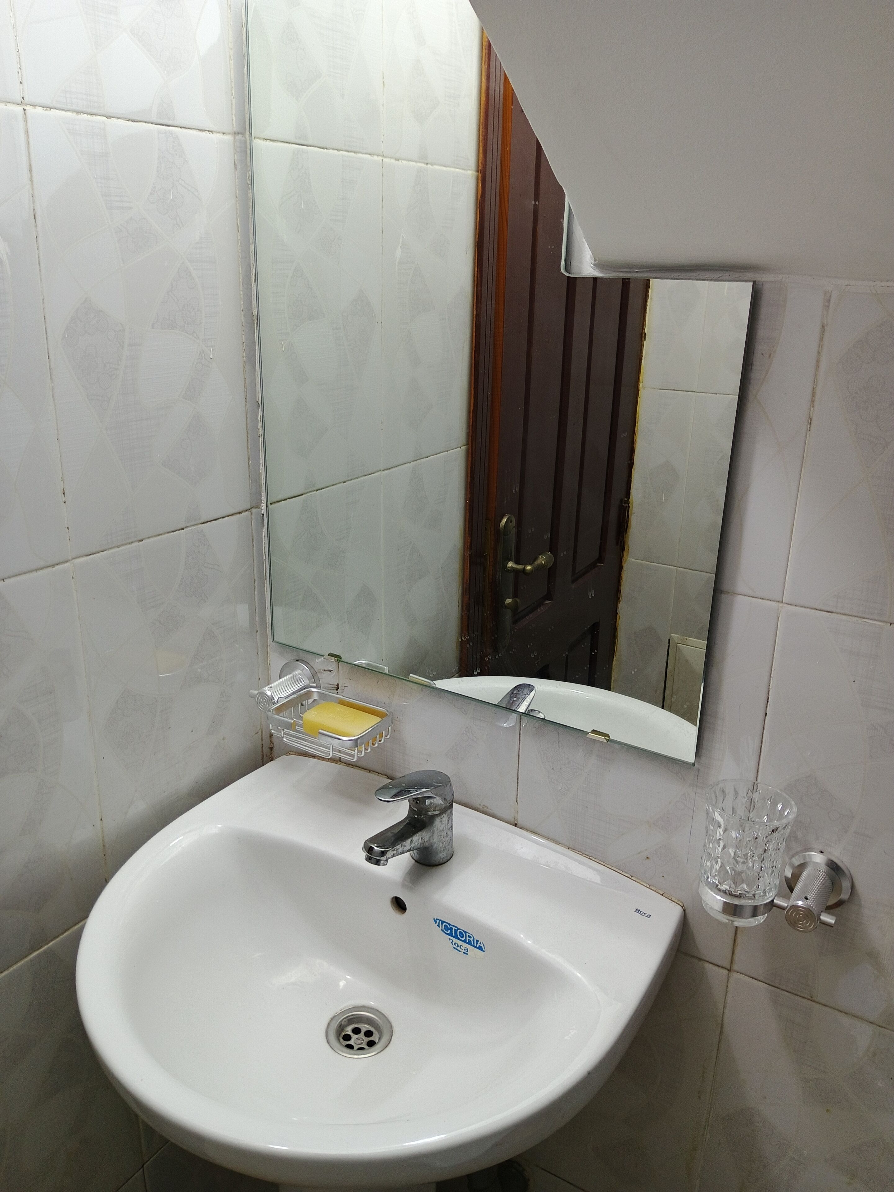 A bathroom with a white sink, a mirror, and a glass soap dish.