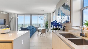 A modern kitchen with a large island, a dining area with a view, and a living room with a sofa and a TV.