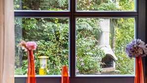 A window with a view of a garden, a stone structure, and two orange vases with flowers. - Studio '38 sqm' with Terrace, Shared Garden and Wi-Fi (Unterkirnach)