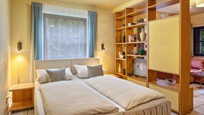 A bedroom with a bed, bedside tables, a window with curtains, a built-in wooden shelf with various items, and a view of the outdoors. - Studio '38 sqm' with Terrace, Shared Garden and Wi-Fi (Unterkirnach)