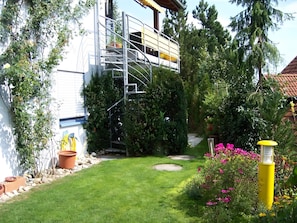 Ein Garten mit einem weißen Gebäude, einer Metalltreppe und einem gelben Laternenpfahl.