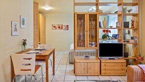 A living room with a wooden dining table, chairs, a TV, and a bookshelf. - Studio '38 sqm' with Terrace, Shared Garden and Wi-Fi (Unterkirnach)