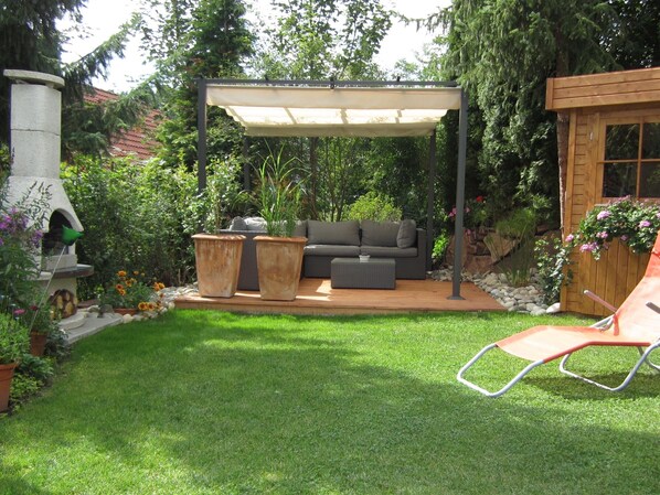Eine Terrasse mit überdachter Sitzecke, einem Grill und einem Rasen.