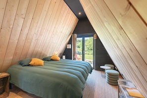 Una habitación acogedora con techo inclinado, una cama con ropa de cama verde, una mesita y vistas a zonas verdes.