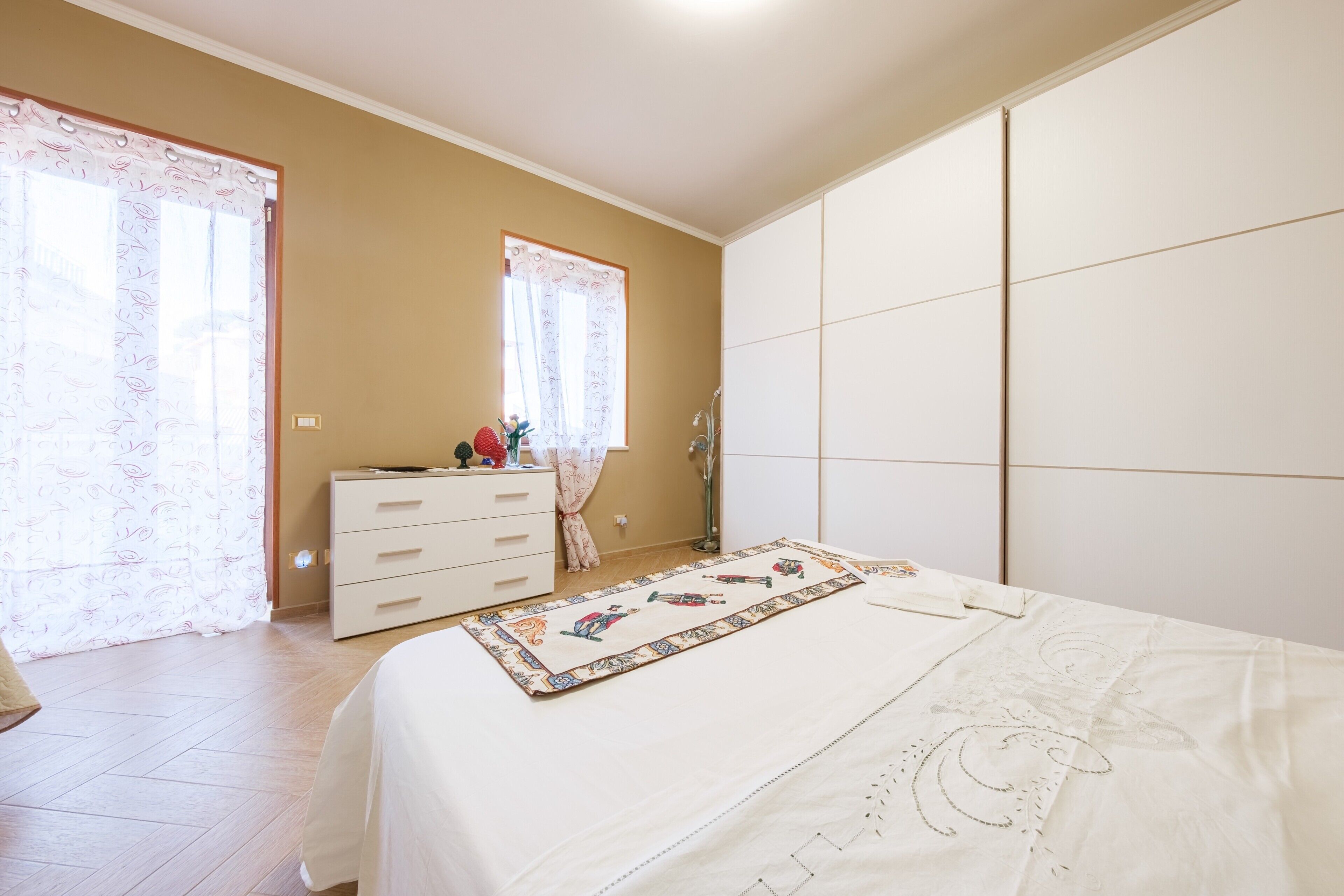 A bedroom with a bed, a dresser, a window with curtains, and a wardrobe.