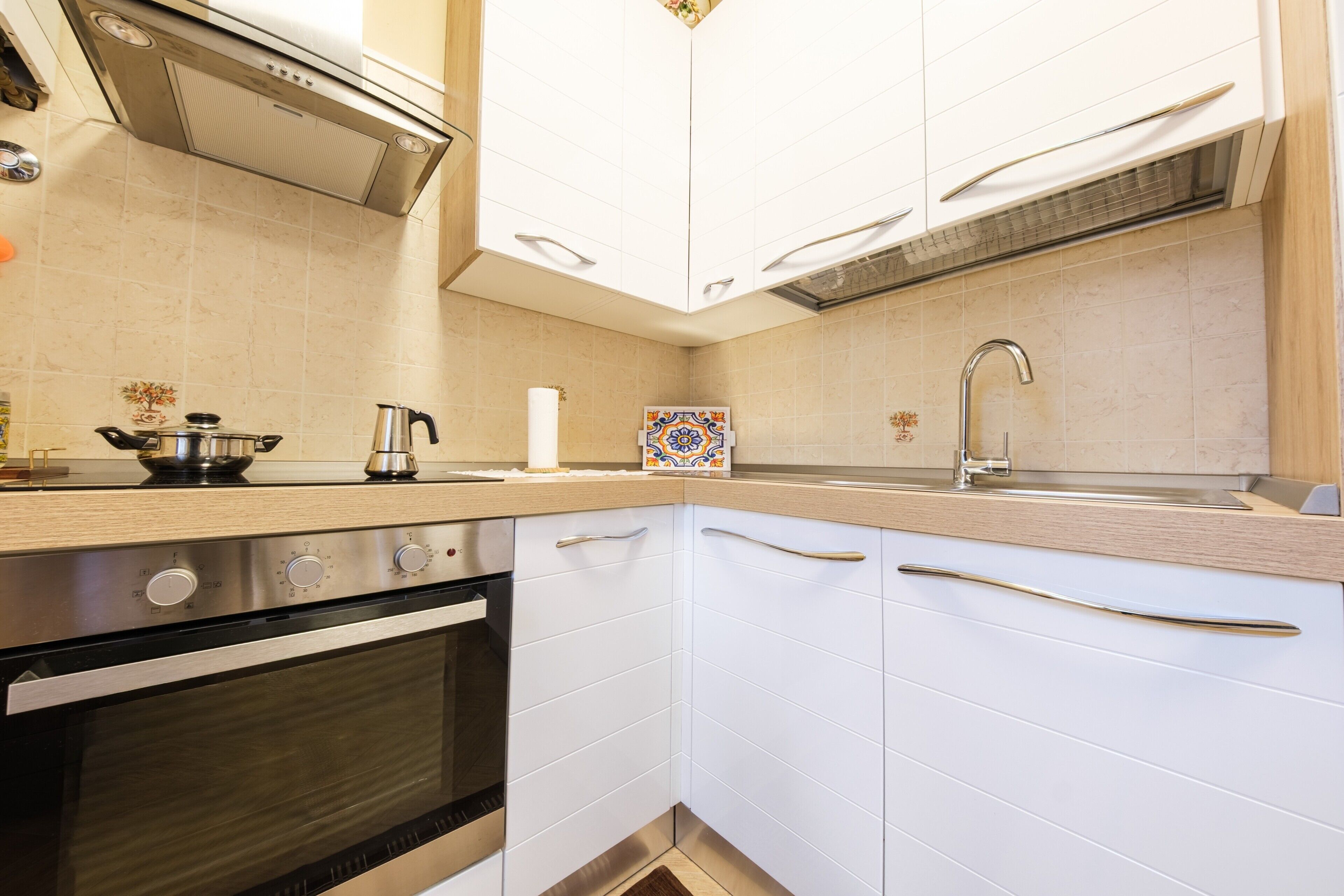 Uma cozinha com armários brancos, forno de aço inoxidável, pia e backsplash de azulejos decorativos.