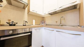 Uma cozinha com armários brancos, forno de aço inoxidável, pia e backsplash de azulejos decorativos.