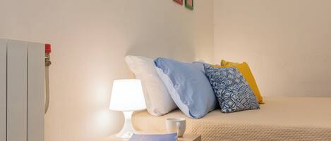 A neatly made bed with pillows, a bedside table with a lamp and a book, and a wall with framed pictures.