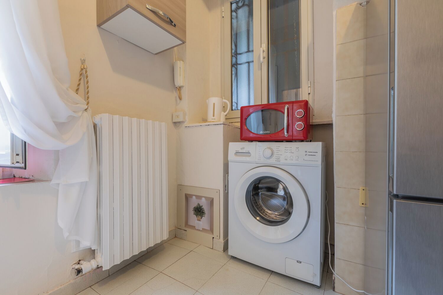 A compact laundry room with a washing machine, a microwave, and a radiator.