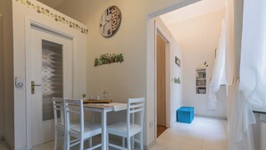 Une pièce avec une table et des chaises blanches, une horloge au mur et une boîte de rangement bleue.