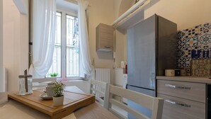 Une cuisine moderne dotée d’un réfrigérateur encastré, d’une table à manger en bois agrémentée d’une plante et d’une fenêtre ornée de rideaux blancs.