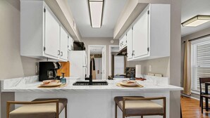 A modern kitchen with white cabinetry, a central island with bar stools, and a built-in oven. - Dog friendly 1st floor  King bd in Ocean Ridge (Edisto Island)