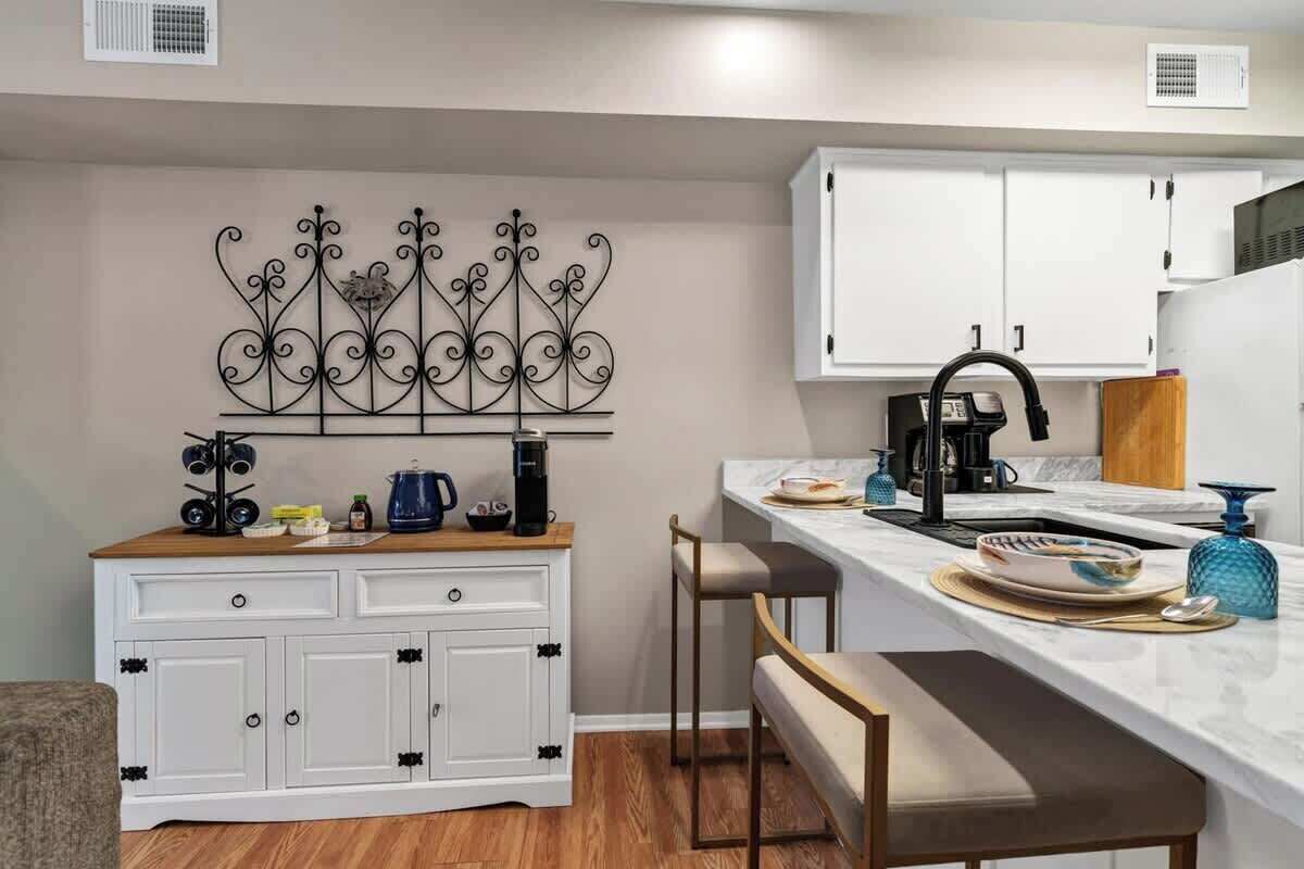 A compact kitchen with white cabinets, a marble countertop, a coffee maker, and a decorative metal wall piece.