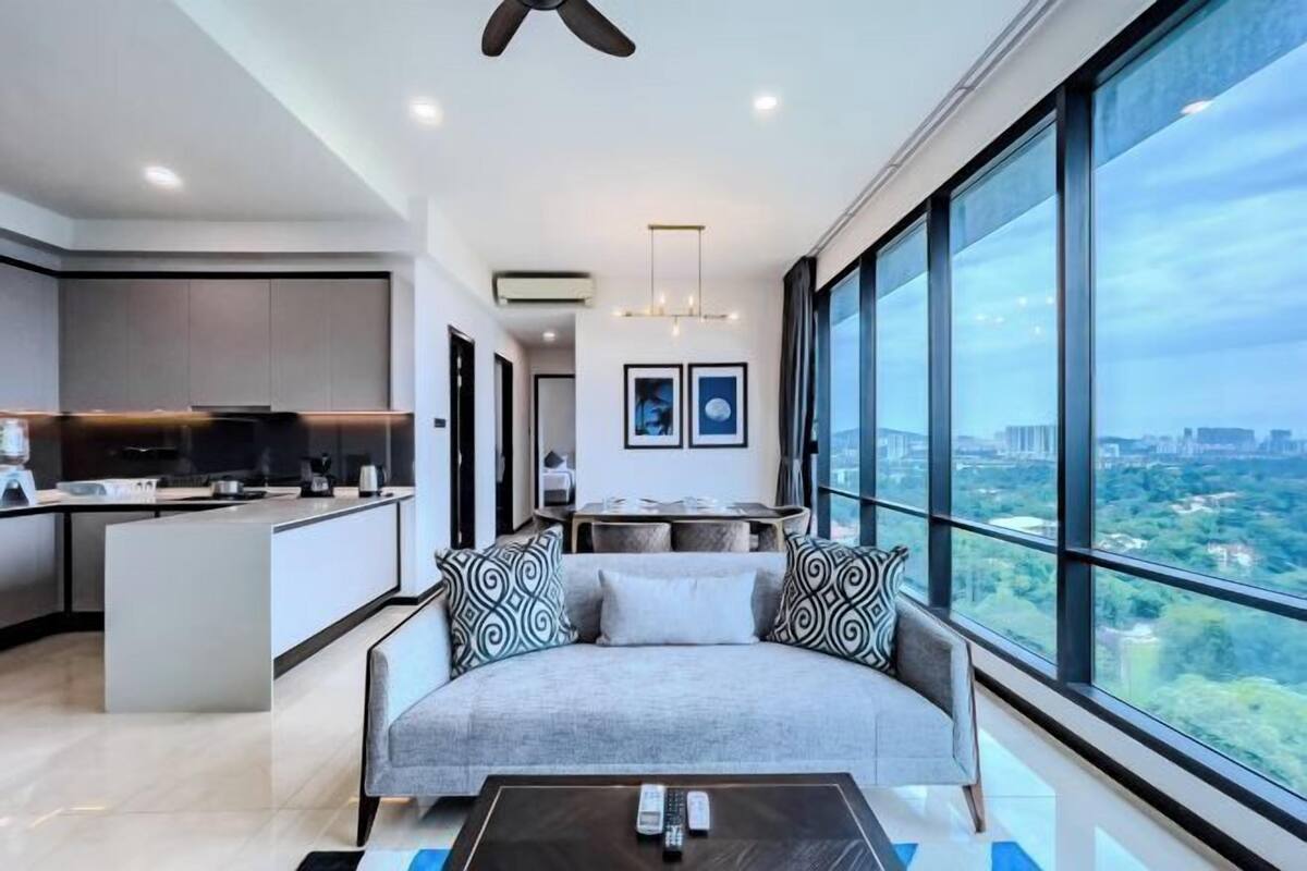 Una sala de estar moderna con un sofá, una mesita de centro y vistas a un paisaje urbano a través de amplios ventanales.