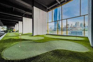 Een indoor golf putting green met uitzicht op de stad door grote ramen.