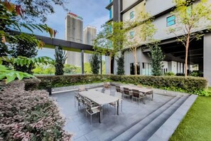 Een buitenpatio met tafels en stoelen, omgeven door groen en een uitzicht op een stadsbeeld.