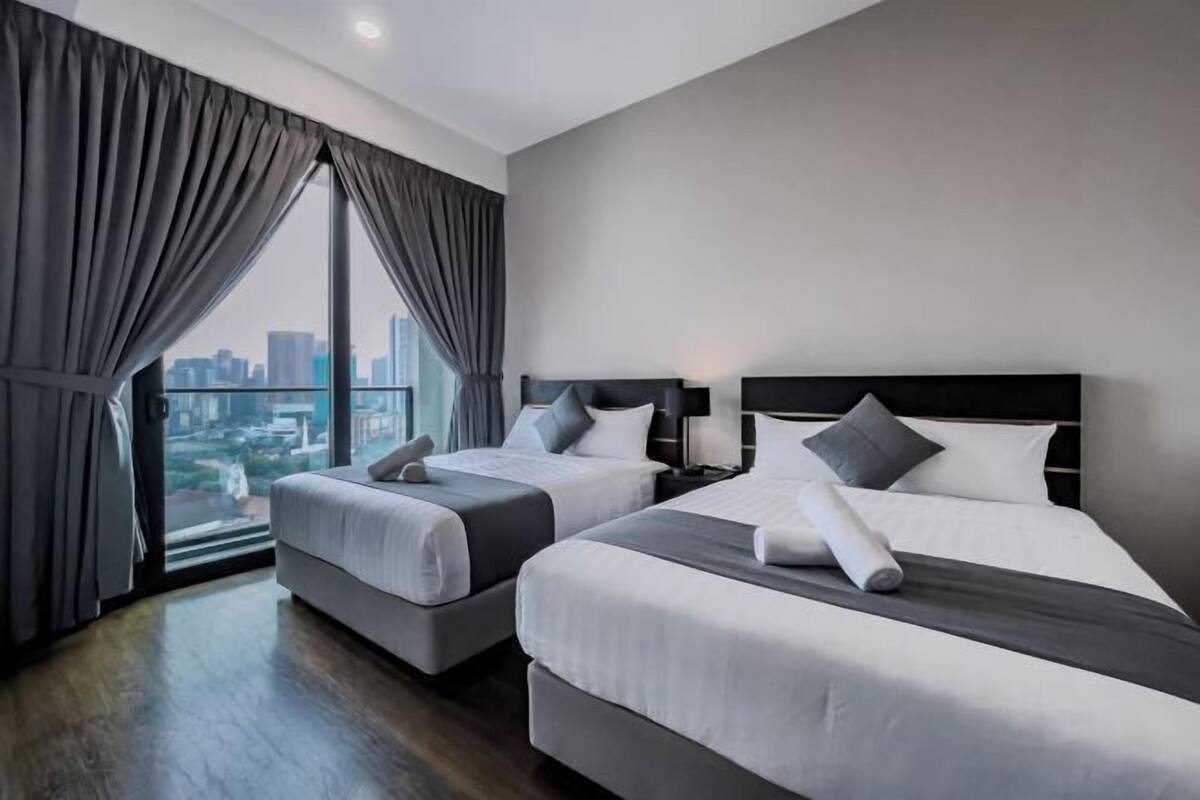 Habitación de hotel con dos camas, vistas a la ciudad y un ventanal con cortinas.