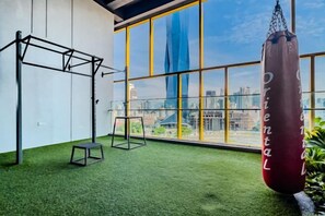 Une salle de sport équipée d’un sac de frappe, de matériel d’exercice et offrant une vue sur le paysage urbain grâce à de grandes fenêtres.