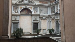Une cour intérieure à l’architecture classique, comprenant des colonnes, une arche centrale et un plafond orné de fresques.