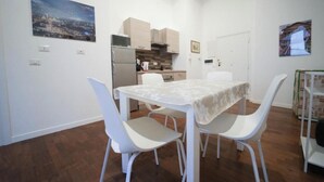Un espace repas avec une table et des chaises, une cuisine en arrière-plan et une vue sur le paysage urbain.