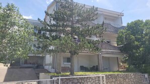 Une maison à deux étages avec une façade en pierre, un porche couvert et un grand arbre dans le jardin.