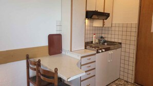 Une petite cuisine avec un seul plan de travail, un évier et une cuisinière. On y trouve une chaise en bois et un meuble contenant un four à micro-ondes.