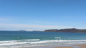 A beach with clear blue water, gentle waves, and distant hills.