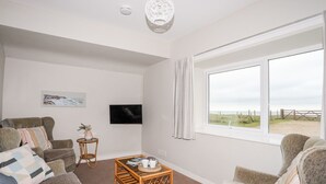 A living room with a large window, a flat-screen TV, and a wicker coffee table. - Ceiriad - 9 Ty'n Don (Pwllheli)