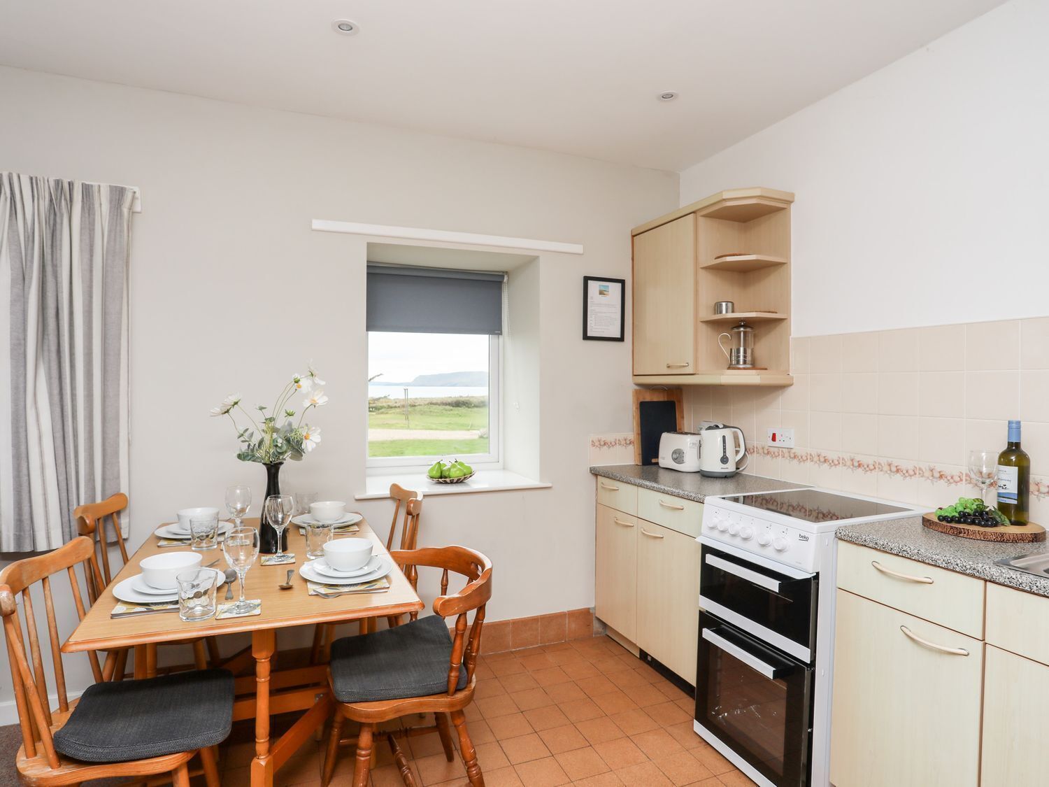 Una cocina con una mesa de comedor preparada para cuatro, una ventana con vistas, microondas, hervidor y lavavajillas.