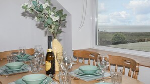 A dining table set for six with green plates and wine glasses, a bottle of champagne, and a vase with white flowers. - Ysgo - 6 Ty'n Don (Pwllheli)
