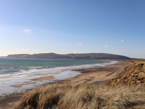 A coastal landscape with a sandy beach, grassy dunes, and a clear blue sky. - Oer - 8 Ty'n Don (Pwllheli)