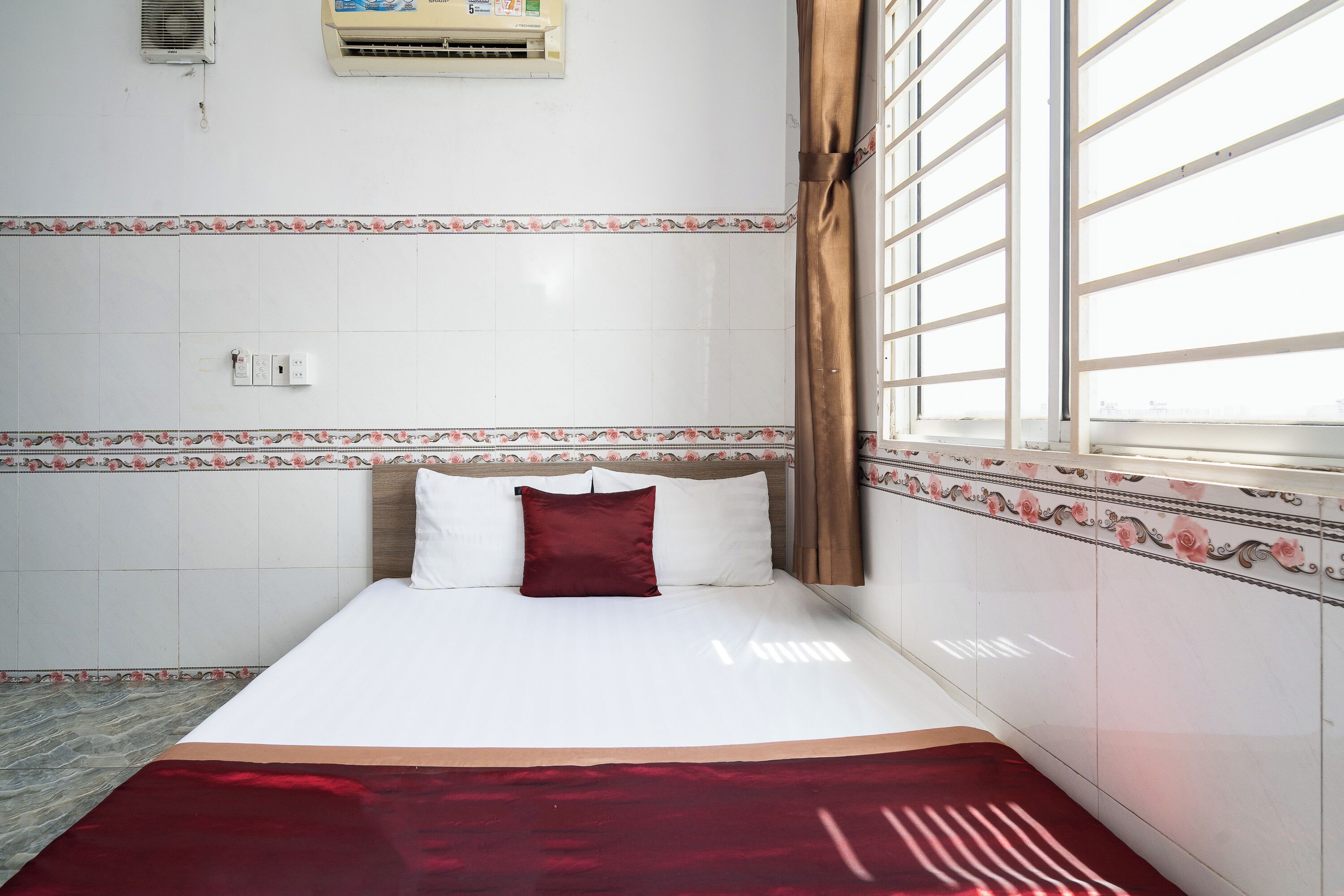 A hotel room with a bed, a window with curtains, and a tiled wall with a floral border.