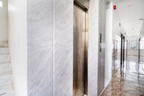 Un pasillo moderno con paredes de mármol y suelo brillante, que conduce a un ascensor.