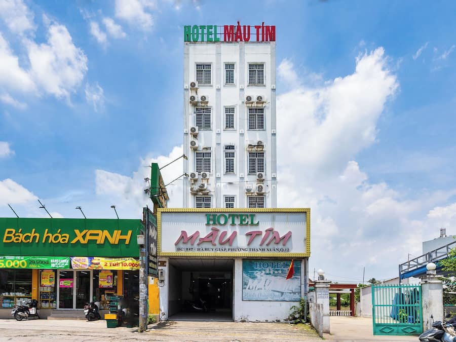Ein Hotelgebäude mit einem Schild, das 'HOTEL MAU TIM' anzeigt, und einer grünen Ladenfassade mit der Beschriftung 'Bách Hóa XANH'.