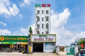 Een hotelgebouw met een bord waarop 'HOTEL MAU TIM' staat en een groene gevel met de tekst 'Bách Hóa XANH'.