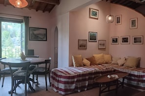 Una habitació amb llit, taula, cadires i finestra amb cortines.