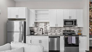 Una cocina moderna con gabinetes blancos, electrodomésticos de acero inoxidable y salpicadero de azulejos.